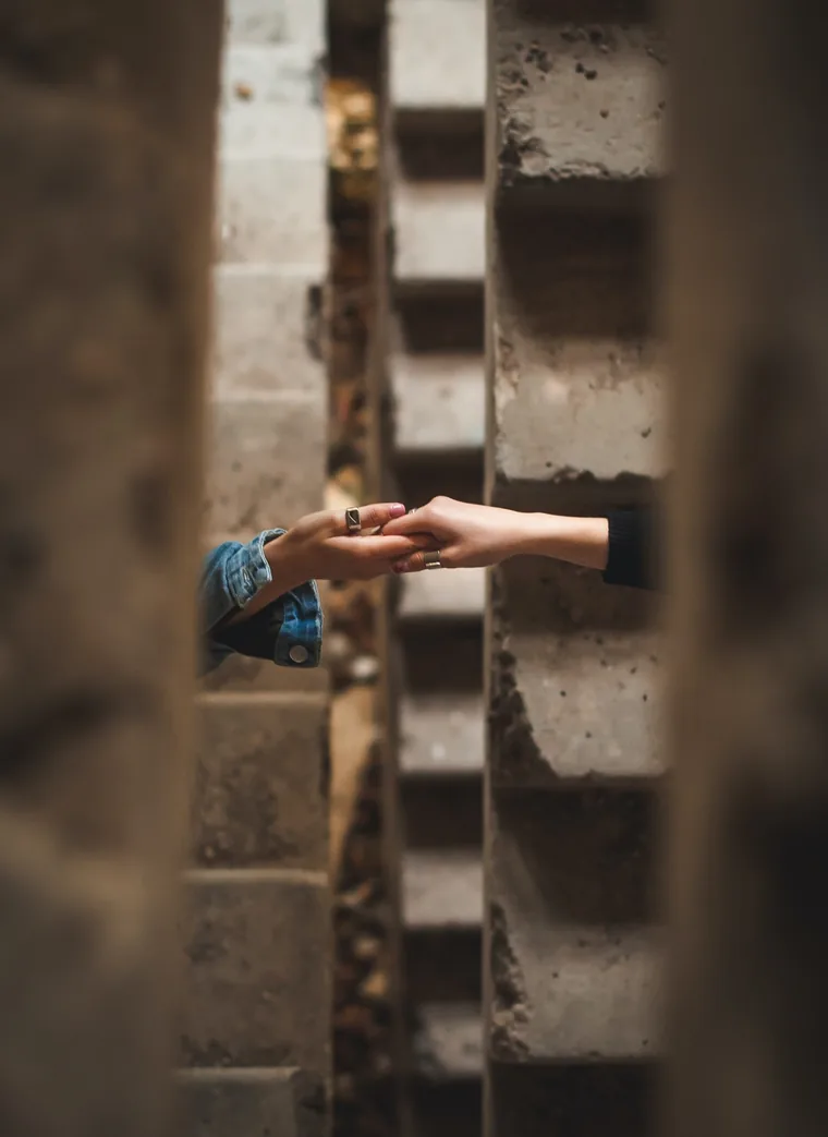 Two people clasping hands through a gap in a concrete wall